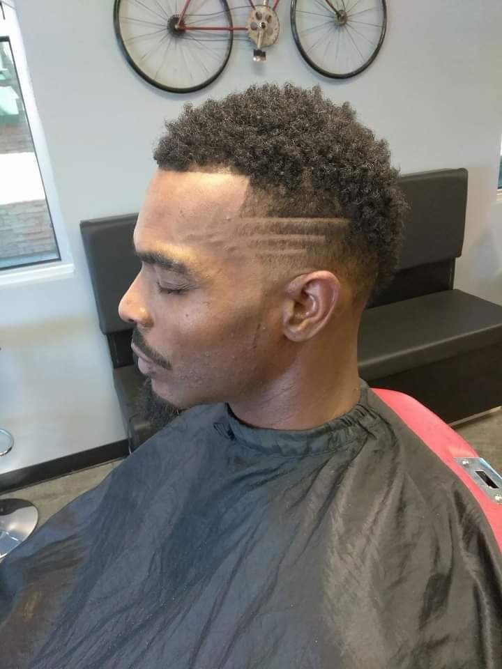 Side profile of a man with a curly top, fade and etched hair design lines